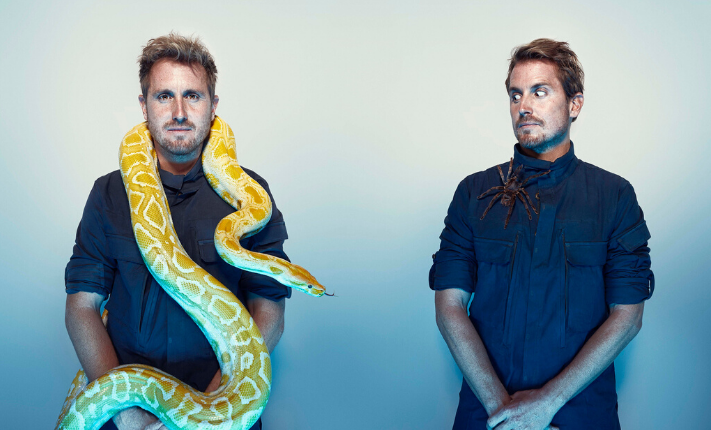 A man with a yellow snake on his neck and another man with a large spider on his shoulder